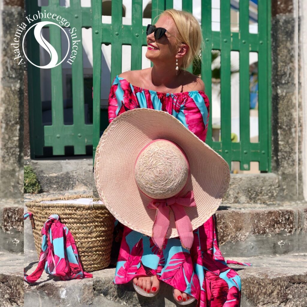 Natalia Ryńska w różowej zwiewnej sukience siedząca na schodach z kapeluszem w ręce